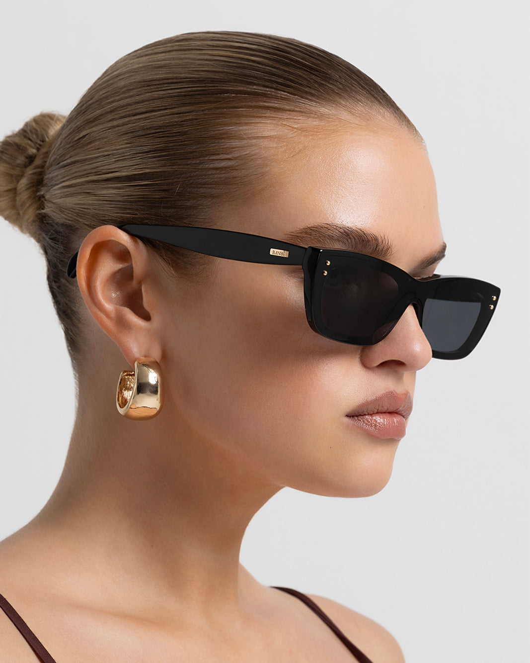 Women’s black rectangular sunglasses with UV protection, chunky acetate frame and subtle gold-tone hardware accents, side view on model.