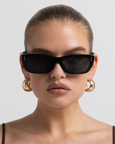 Women’s black rectangular sunglasses with UV protection, chunky acetate frame and subtle gold-tone hardware accents, front view on model.