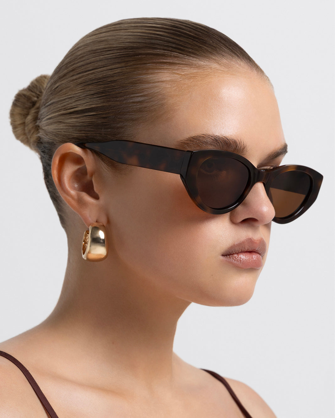 Women’s tortoiseshell cat-eye sunglasses with UV protection, chunky acetate frame, tinted lenses and wide temples, side view on model.
