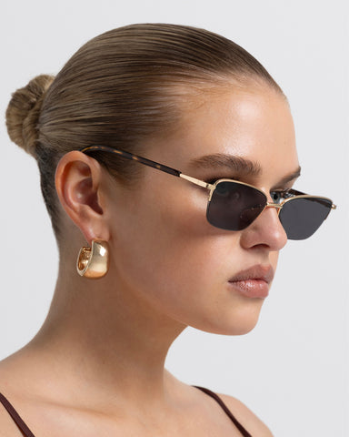 Women’s gold-tone, tortoiseshell metal cat-eye sunglasses with rectangular tinted lenses, thin frame, side view on model
